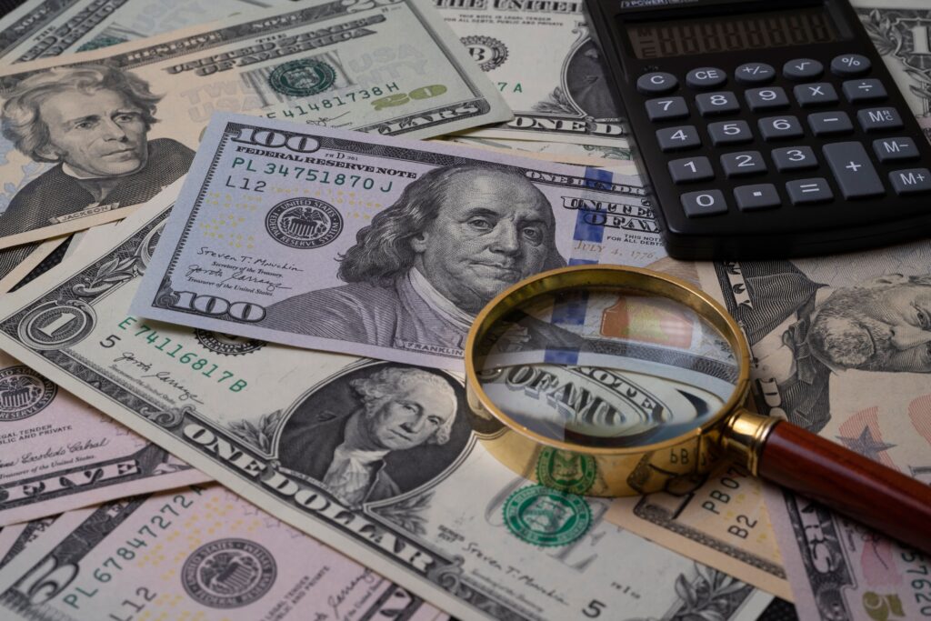 Magnifying glass and calculator examining US dollar bills to check foreign exchange transaction fees