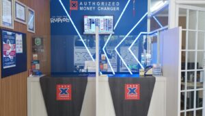Money Changer Exchange Rates displayed at an authorized Cash X Change counter with a visible foreign currency rate board